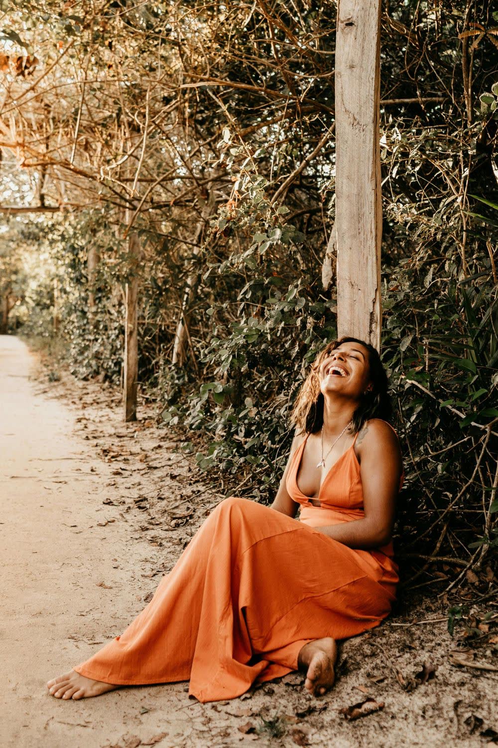 A woman in an orange dress laughing on a sandy path